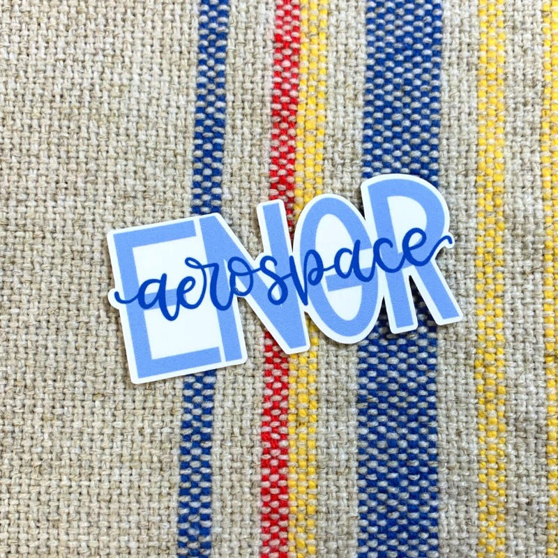 A sticker with the words 'aerospace ENGR' in in blue lettering, sitting on a colorful woven mat. The white background of the sticker makes the blue lettering stand out, drawing attention to the words. This sticker is a great way for aerospace engineers to show their pride and passion for their profession. The colorful woven mat adds a fun and playful touch to the image.